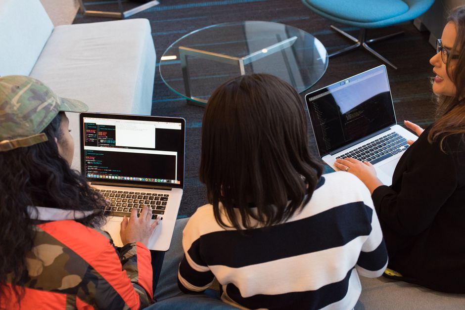 Three people collaborating on laptops showing code in a modern office space